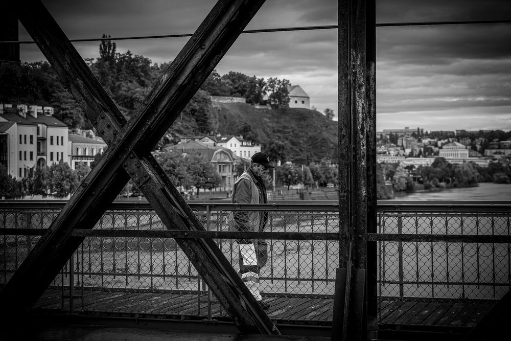 Black and white panoramic photograph showing architectural girders framing an urban waterfront landscape.