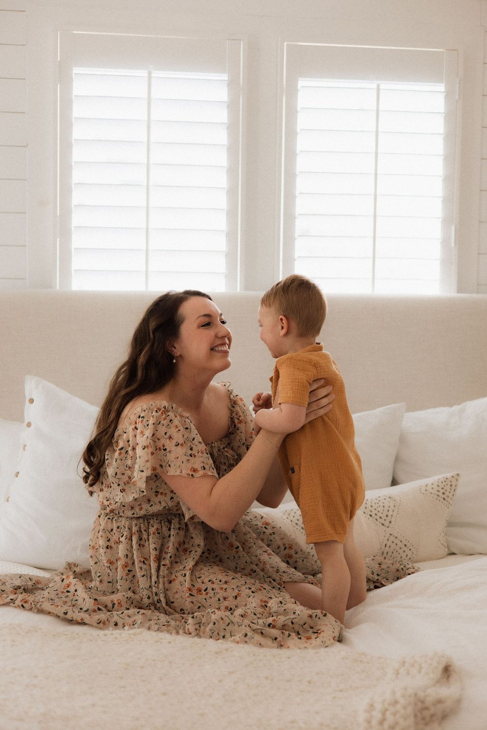 Young family sharing tender moment on white couch with sunlit windows and decorative pillows.