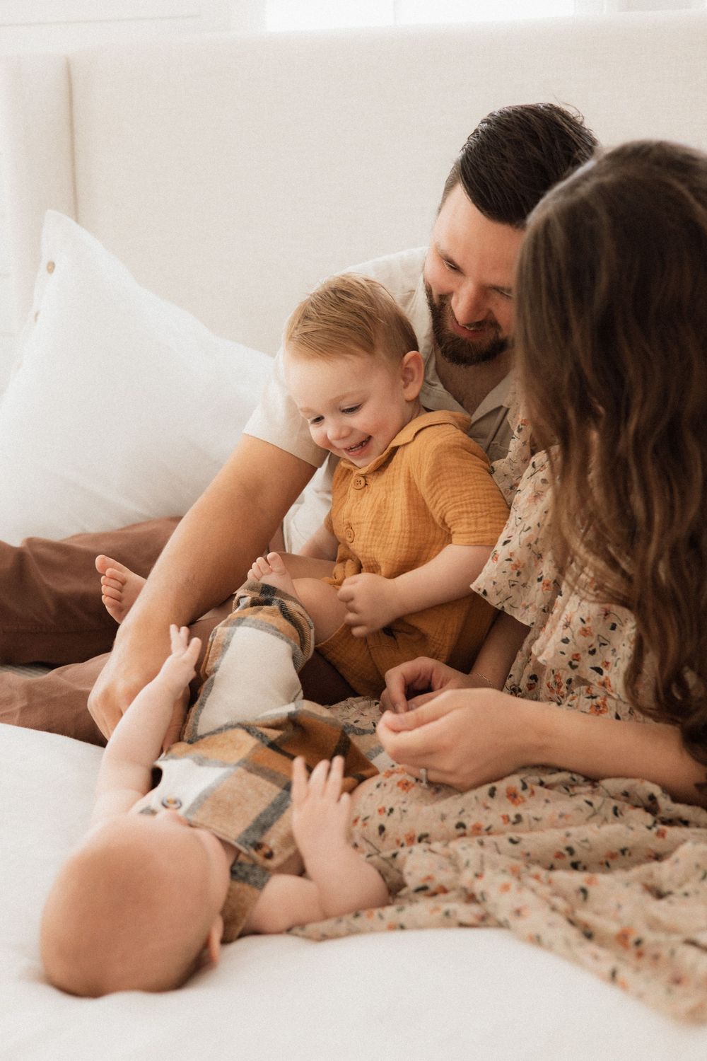 Family enjoying intimate playtime together on a cozy bed with warm natural lighting streaming through the windows.