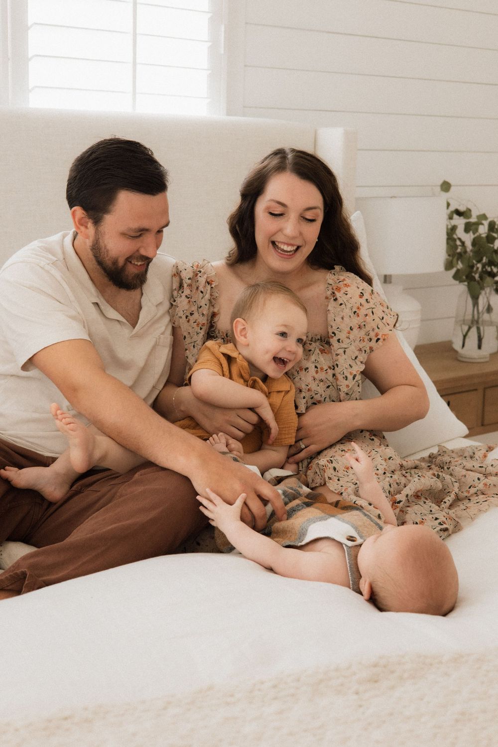 A family enjoys a tender moment together on their bed, sharing laughs and cuddles in a bright white room.