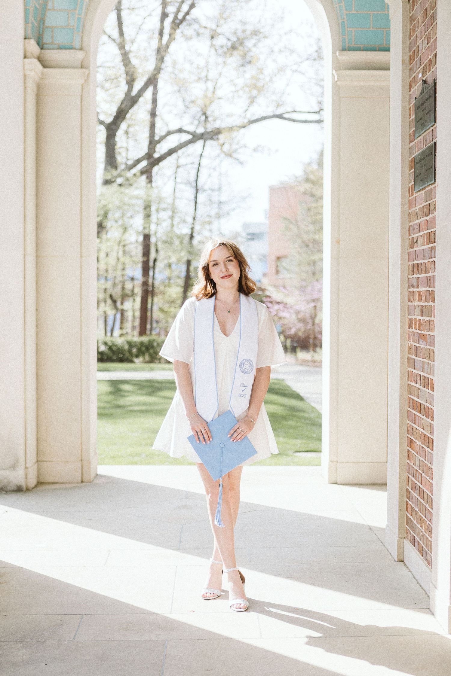 Joyful graduation photo of a senior standing in the arches of the Bell Tower at UNC Chapel Hill with a sweet smile