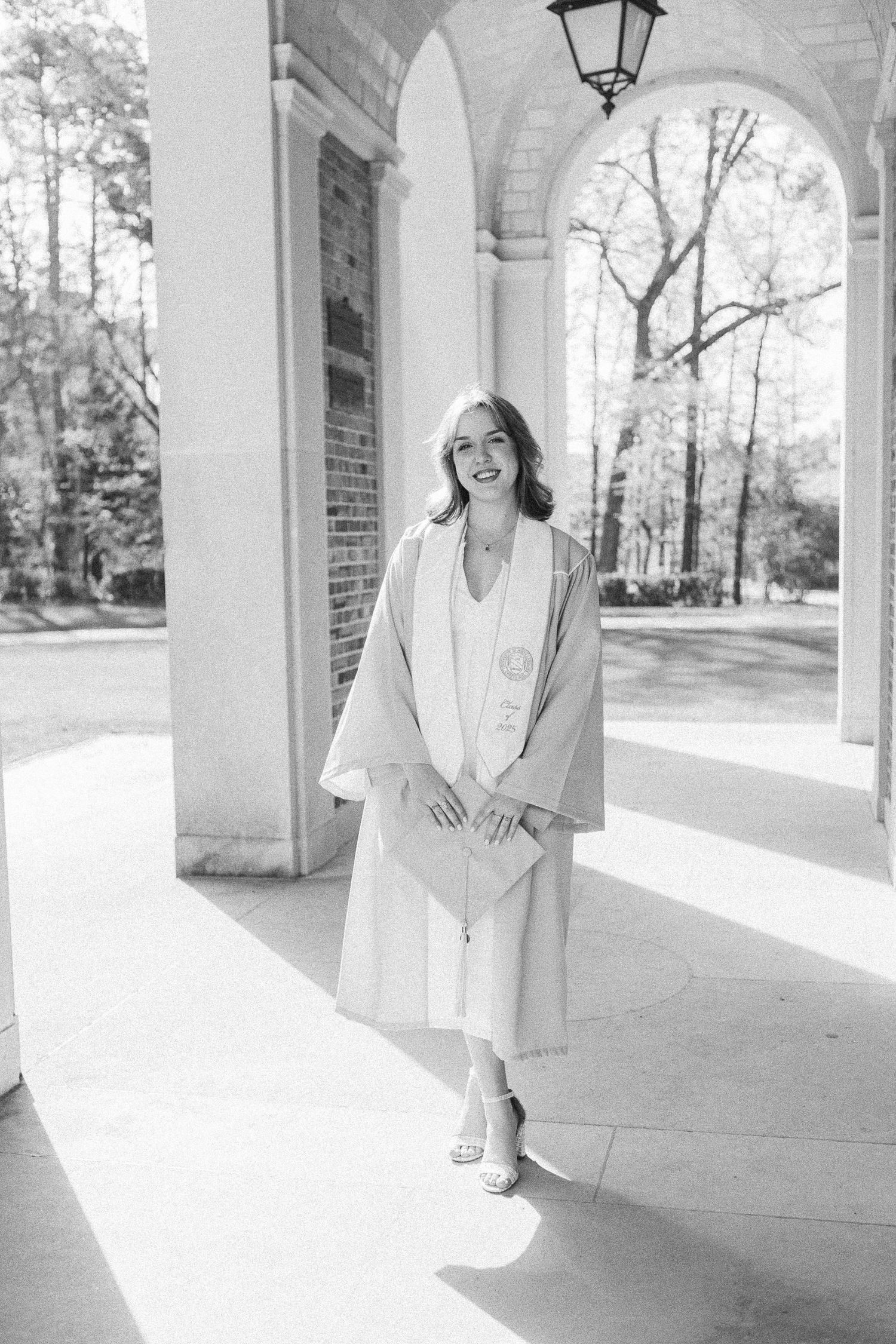 Elegant black and white portrait of a joyful senior in cap and gown beneath the iconic arches of the Bell Tower at UNC Chapel Hill