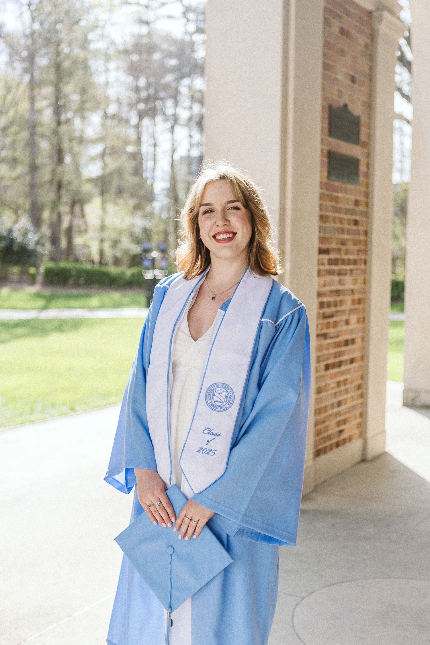 Portrait of a joyful senior in cap and gown beneath the iconic arches of the Bell Tower at UNC Chapel Hill