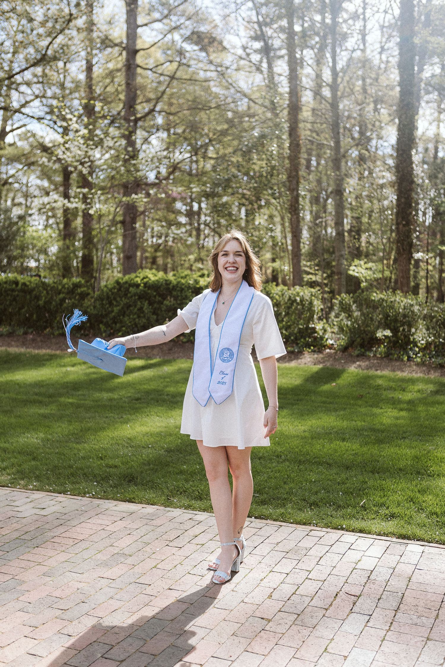 Candid graduation photo of UNC senior tossing her cap beside the Bell Tower