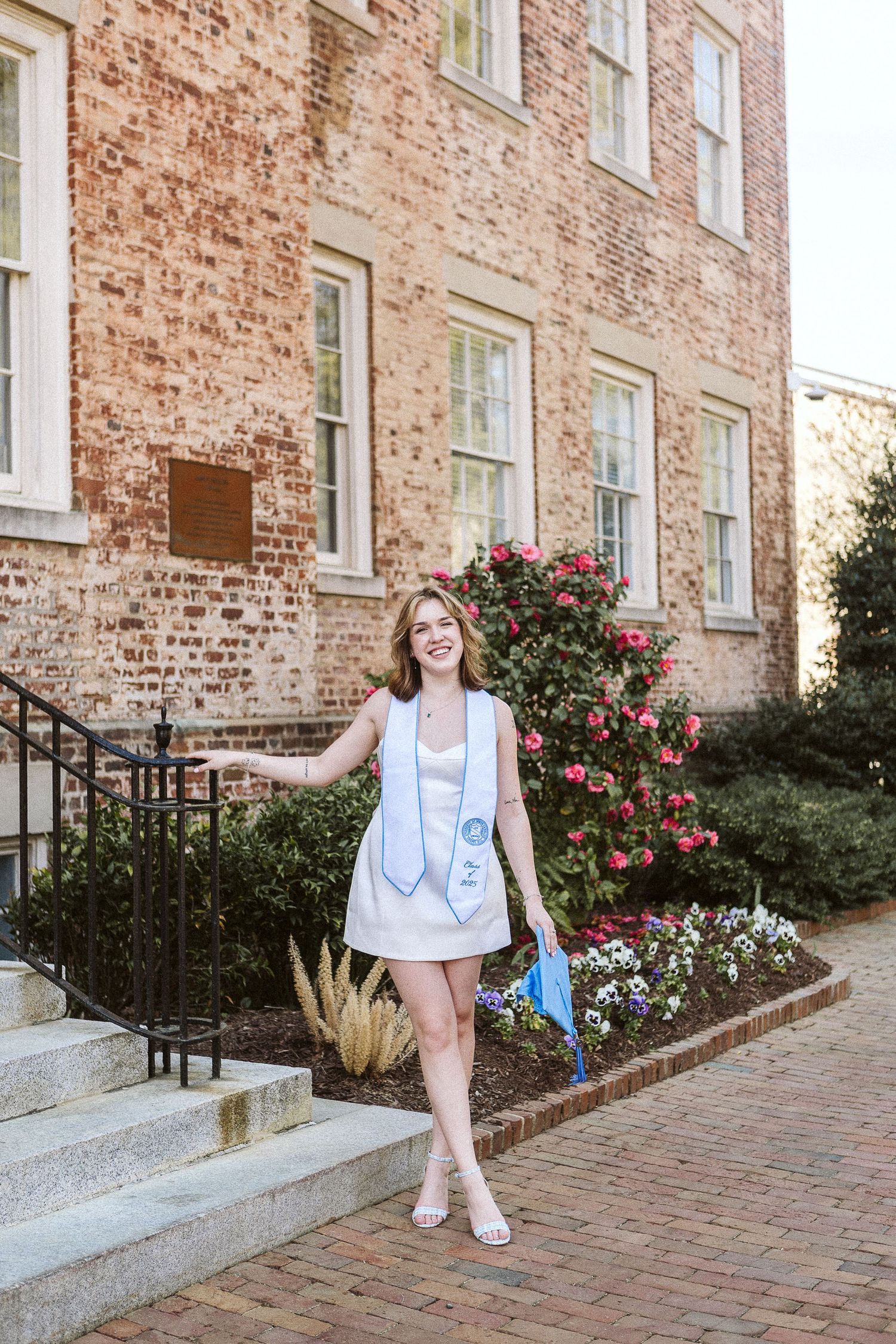 Joyful senior portrait of a UNC Chapel Hill graduate smiling near a brick building and the Old Well