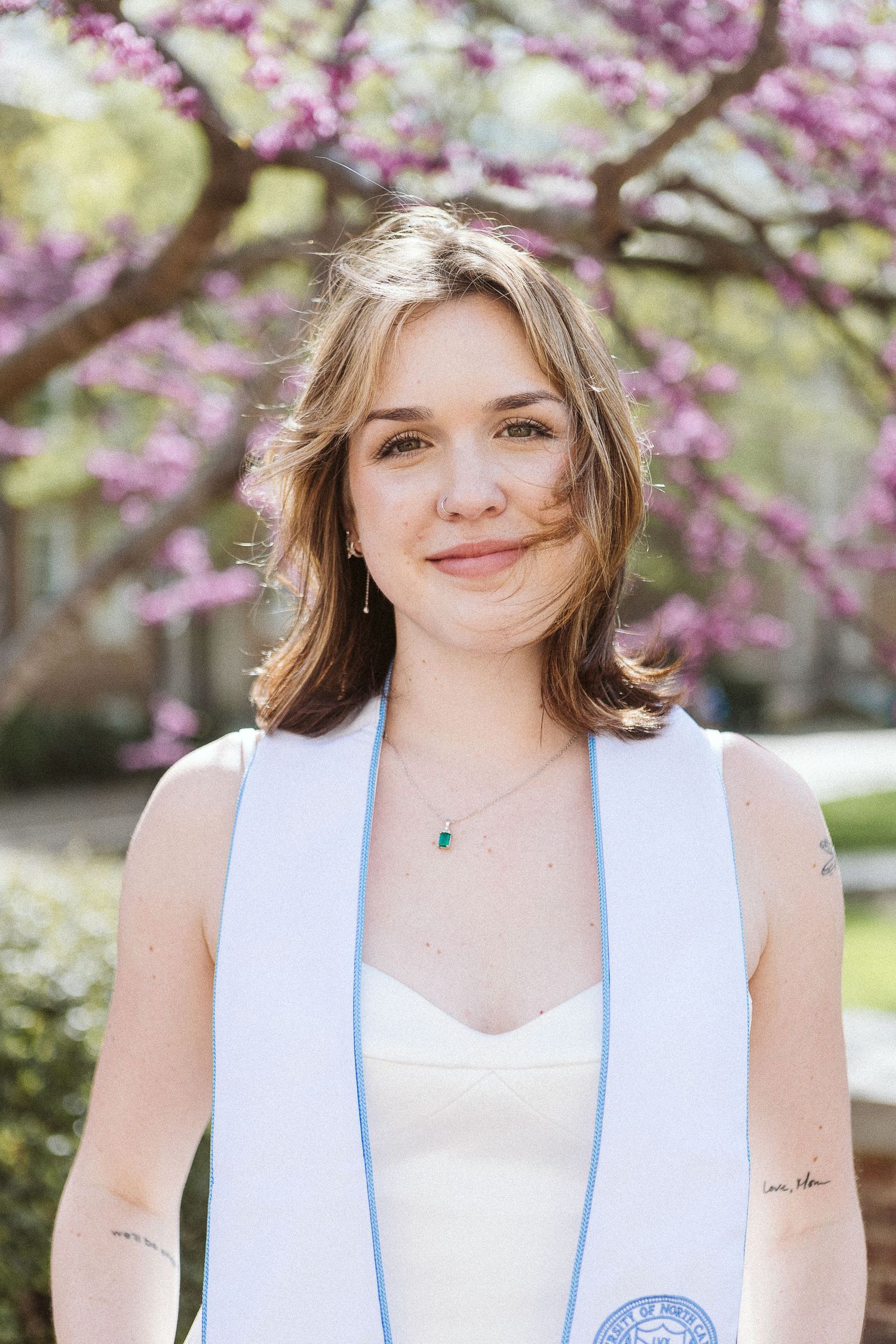 Joyful senior photo of smiling UNC Chapel Hill student under blooming redbuds in natural light