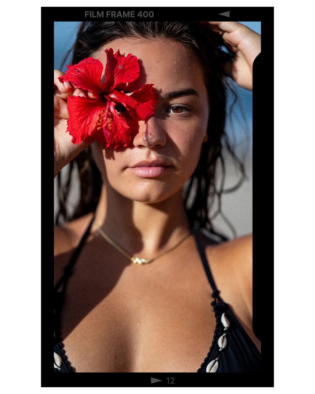 A vibrant red hibiscus flower covers one side of the face as warm sunlight casts shadows in a dramatic portrait.