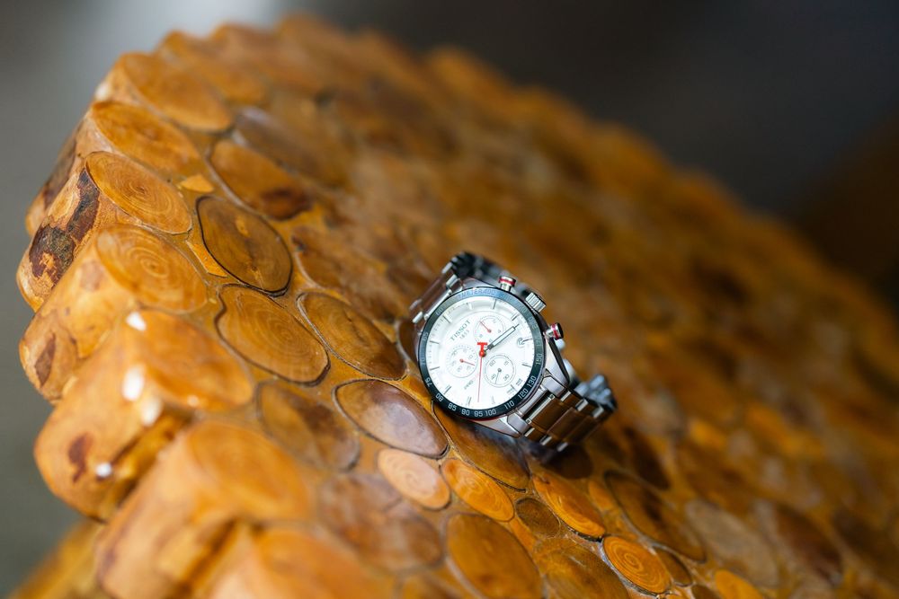 A silver wristwatch displayed on a textured amber-colored surface with intricate patterns.