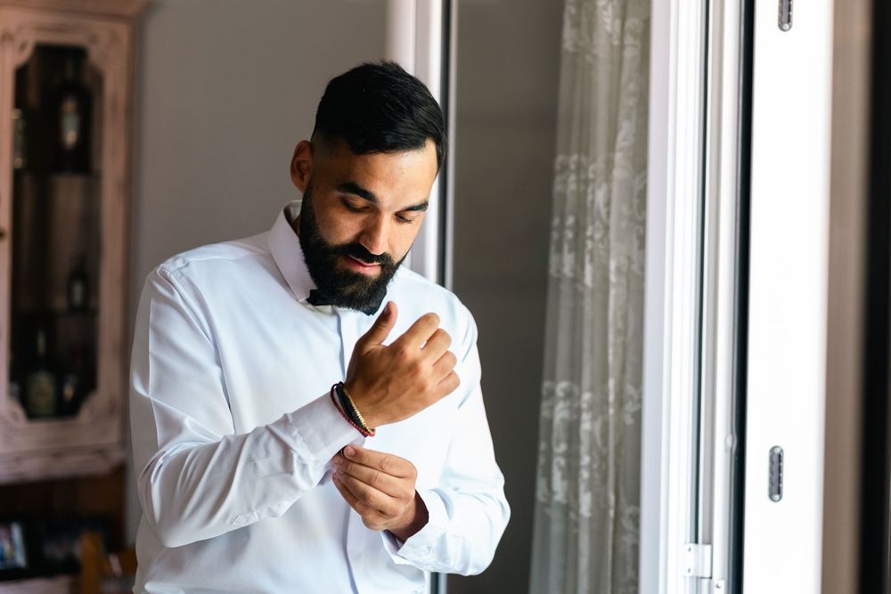 A person buttoning up a crisp white dress shirt while preparing for a formal occasion.
