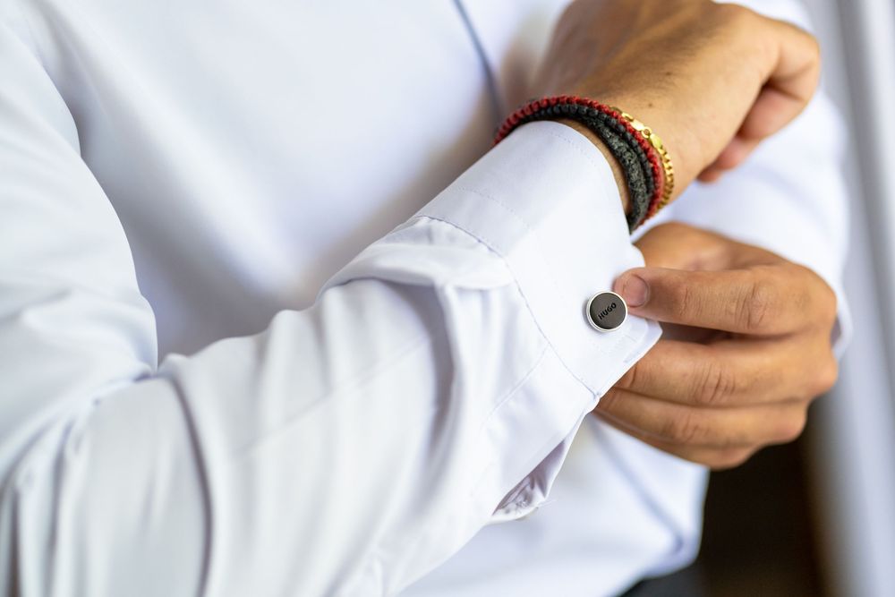 Close-up shot of hands fastening cufflinks on a white dress shirt sleeve.
