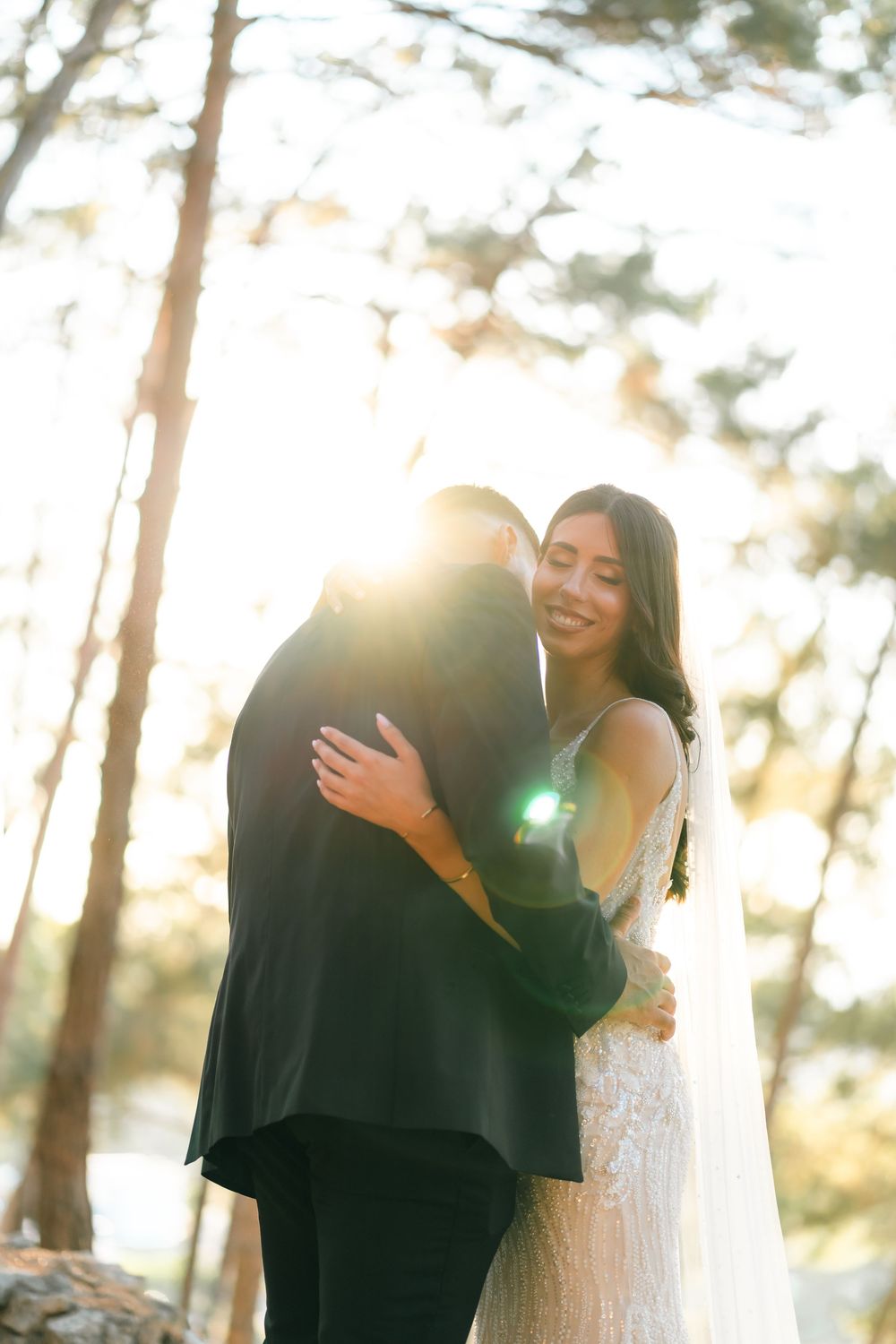 Sunlit wedding portrait of couple embracing among pine trees.
