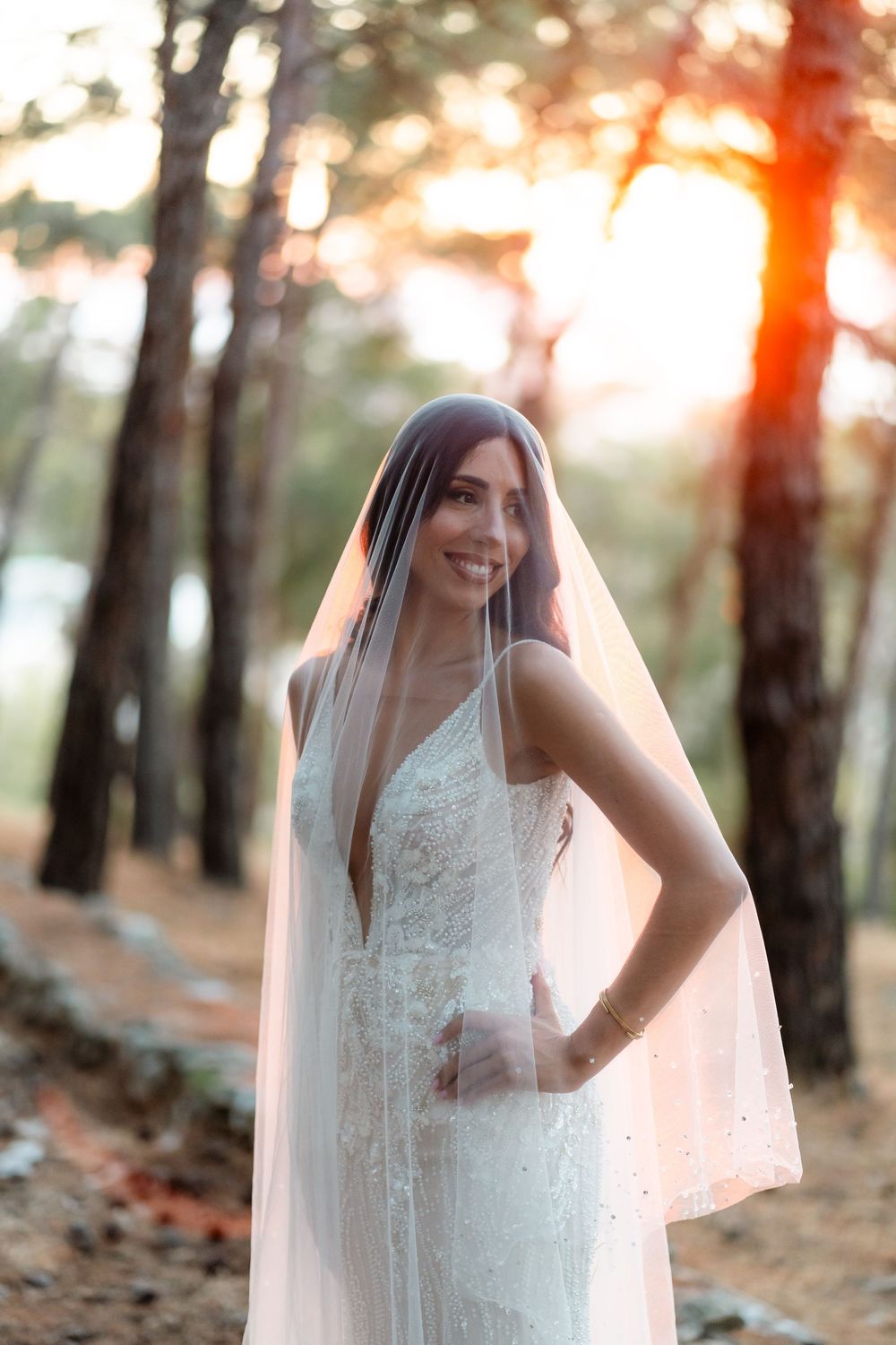 A bride in a fitted lace wedding dress poses in a forest during golden hour.