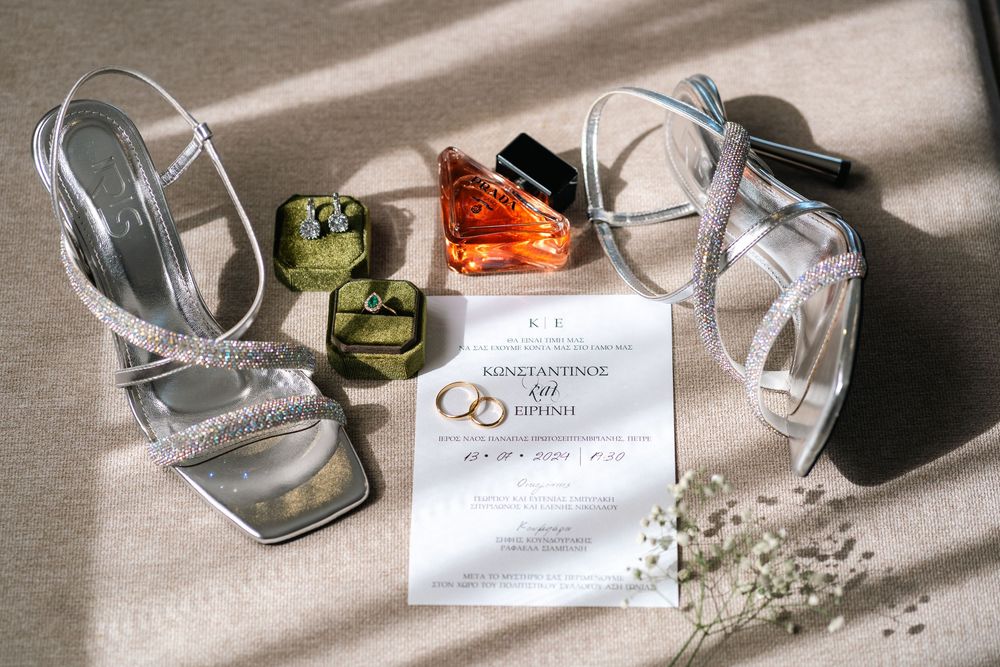 Wedding details including silver heels, perfume bottles, and invitation with interlocking rings symbol.