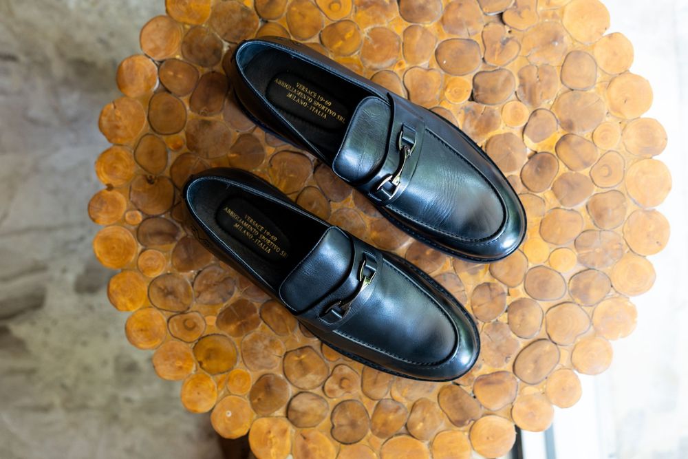 Black leather dress loafers positioned on a wooden hexagonal pattern surface.