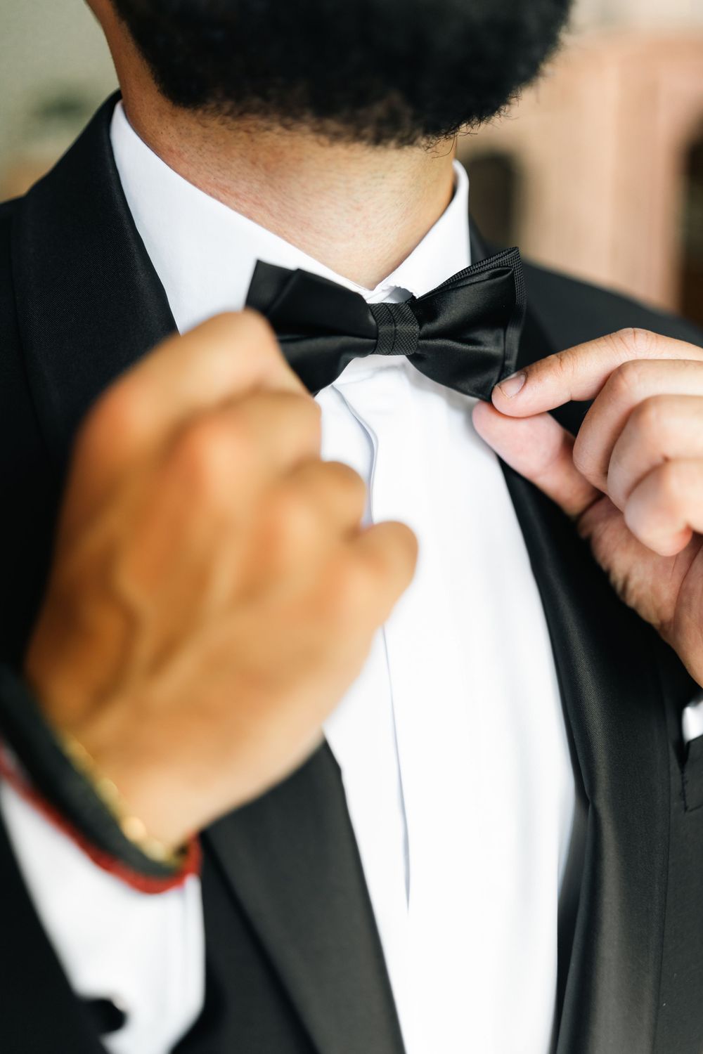 Close-up of hands adjusting a black bow tie on formal attire.