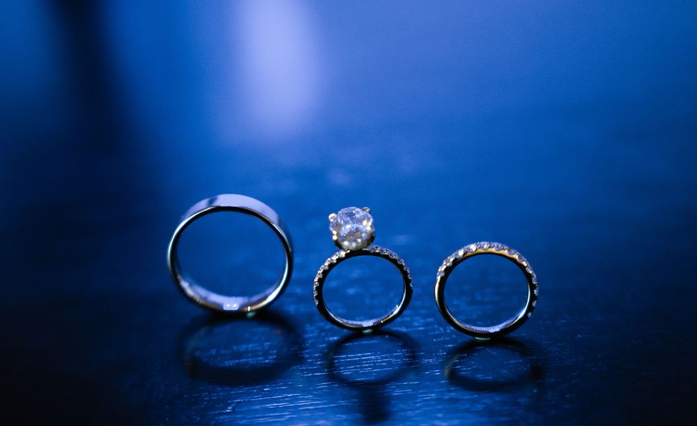 Three elegant wedding rings with diamond details arranged in a row against a dark blue background with reflective surface.