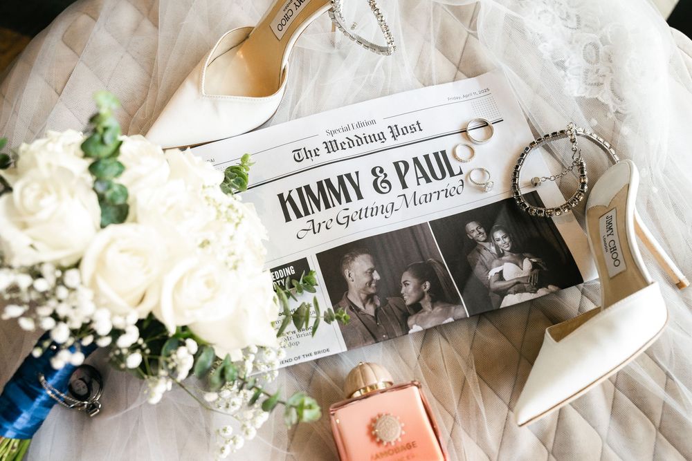 Wedding details flatlay with newspaper clipping, white roses, baby's breath flowers, and vintage photographs.