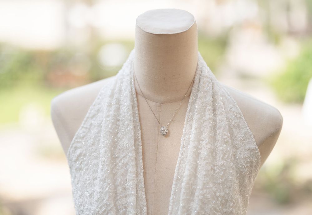 White lace scarf draped on a beige mannequin torso with delicate silver necklace against soft blurred background.