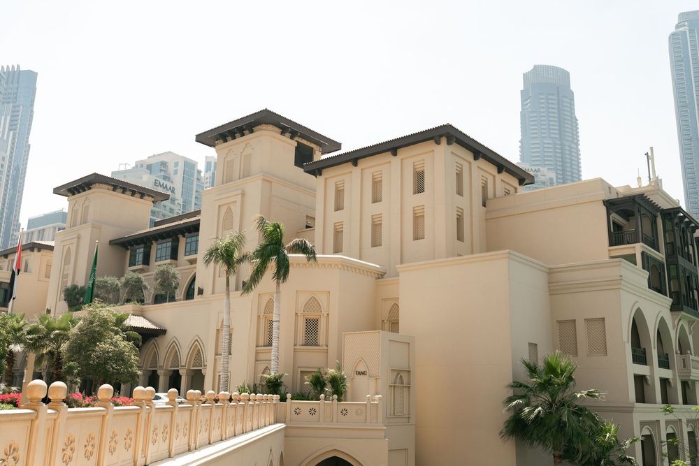 Elegant beige Mediterranean-style building with palm trees and modern skyscrapers visible in the background in Dubai.
