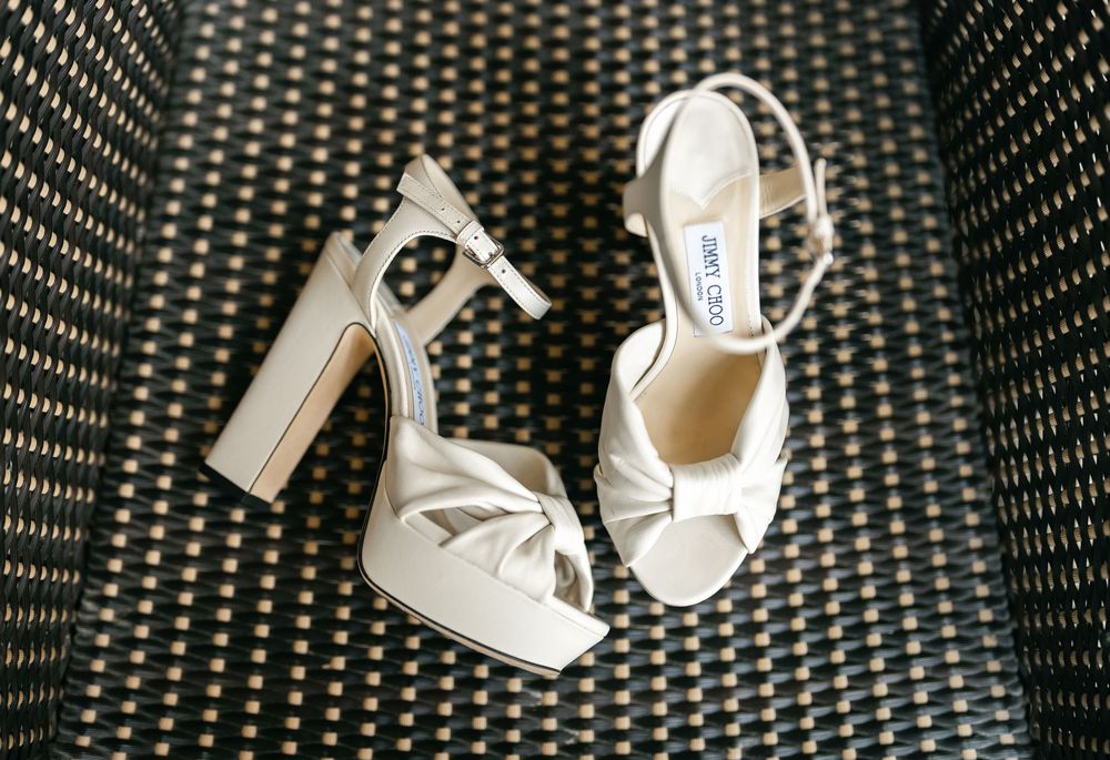 Elegant white satin bridal shoes with chunky heels and knot details displayed on a textured dark background.