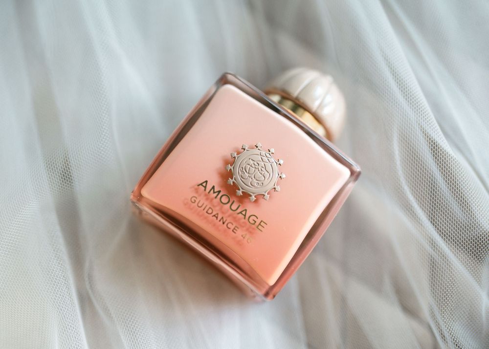 A pink Amouage luxury perfume bottle with ornate silver detailing rests on white tulle fabric.