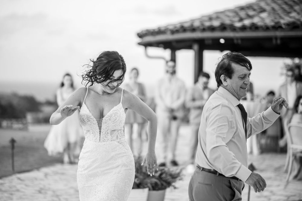Black and white photo of newlyweds dancing joyfully during outdoor reception.