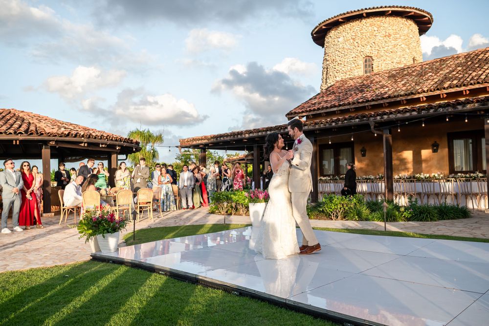 Wedding celebration on an outdoor dance floor with Mediterranean architecture and guests watching.