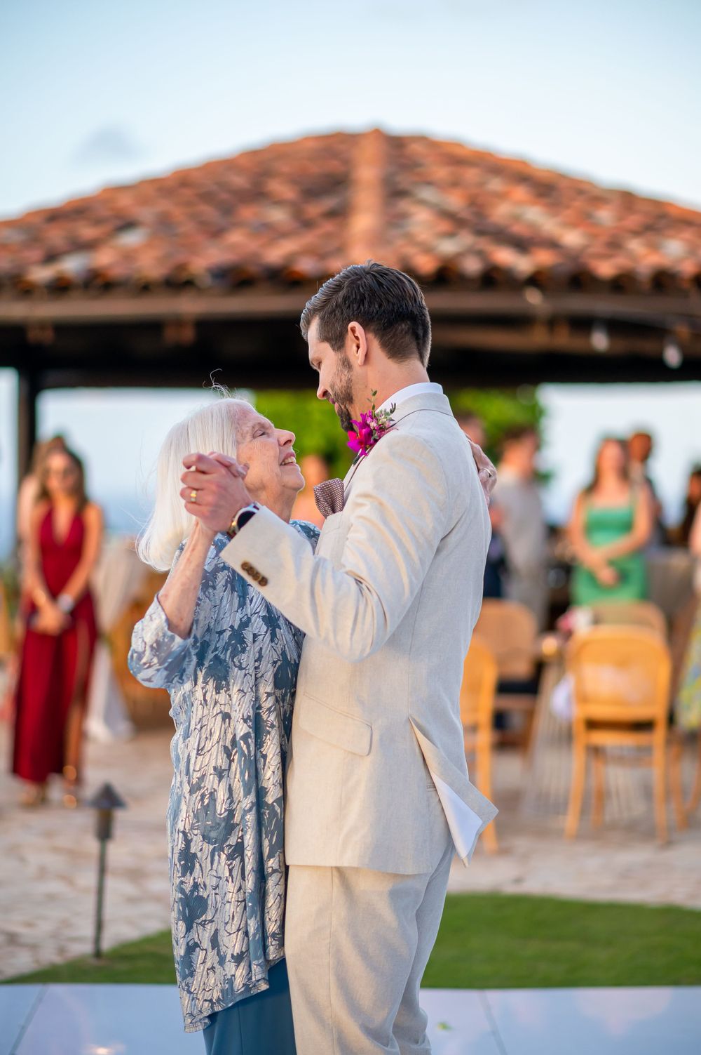 Couple dancing together at an outdoor wedding reception under a terracotta-roofed pavilion.