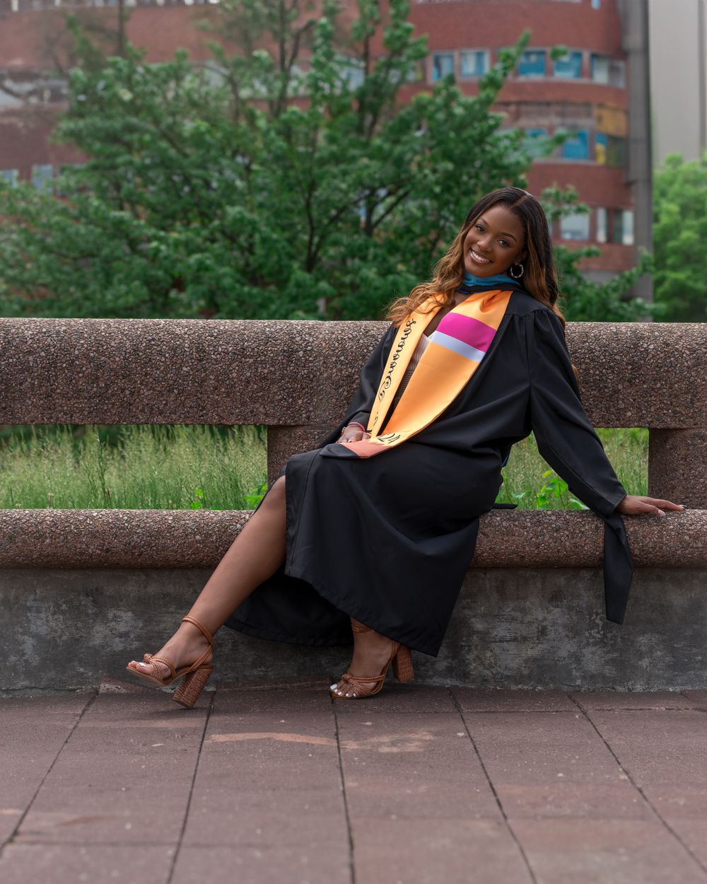 Graduation portrait showing graduate lounging on stone wall in academic dress.