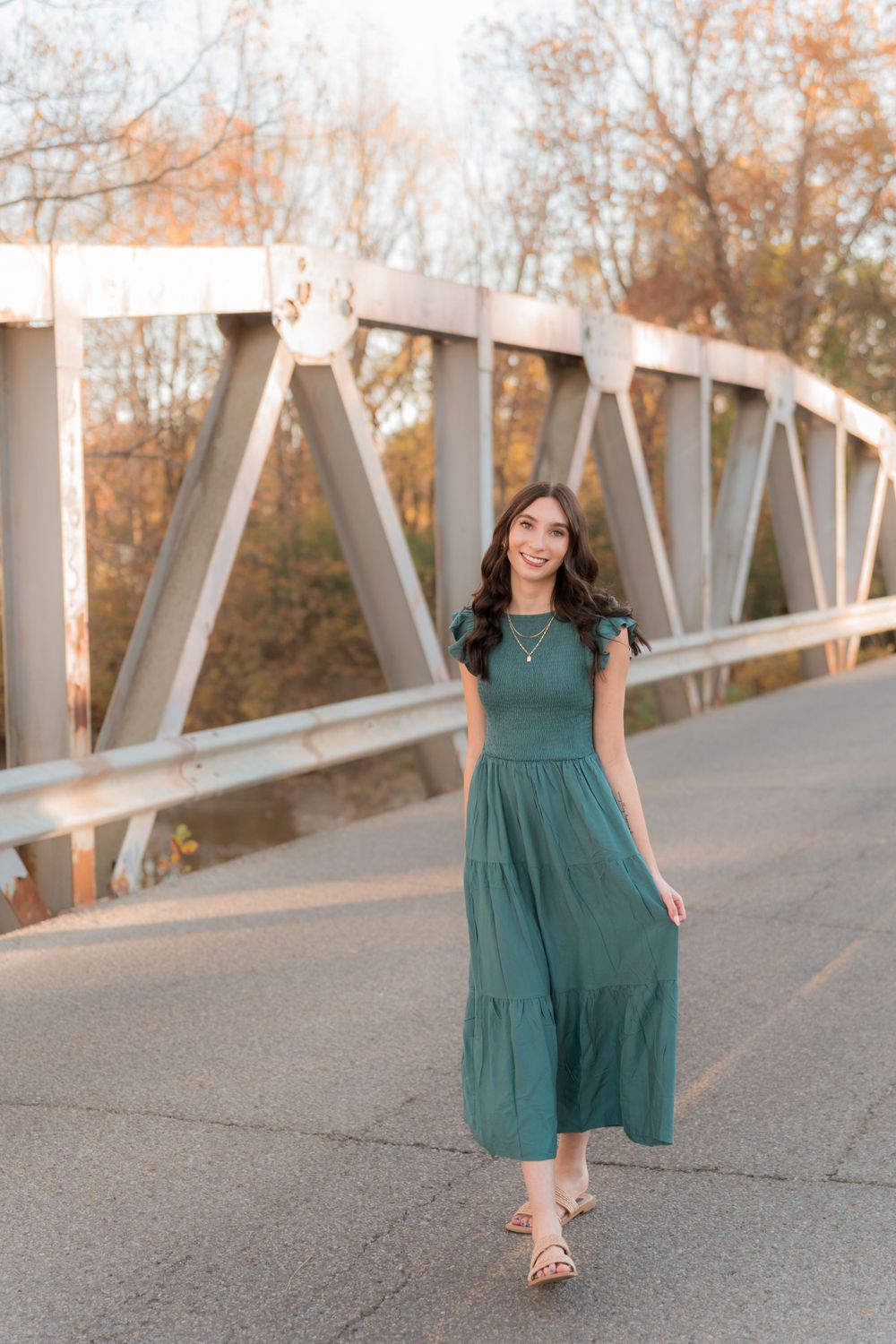 Woman in a flowing green maxi dress walks gracefully across a metal bridge during autumn.