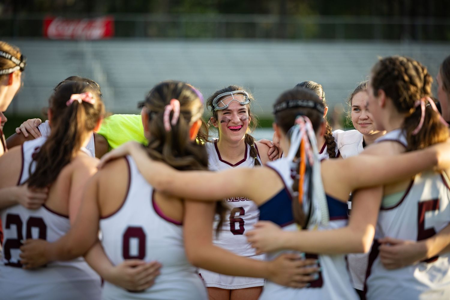 Athletes huddle together celebrating during a sports match with a Coca-Cola sign visible.