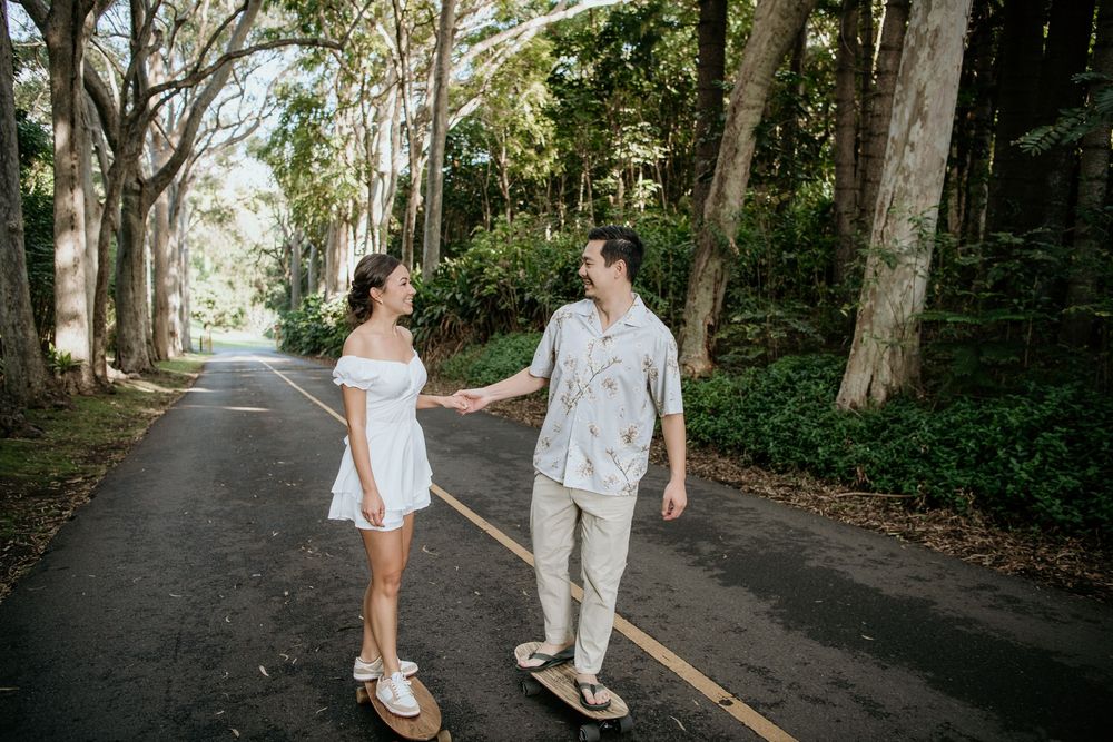 Two figures walk together holding hands on a tree-lined paved road during a sunny day.