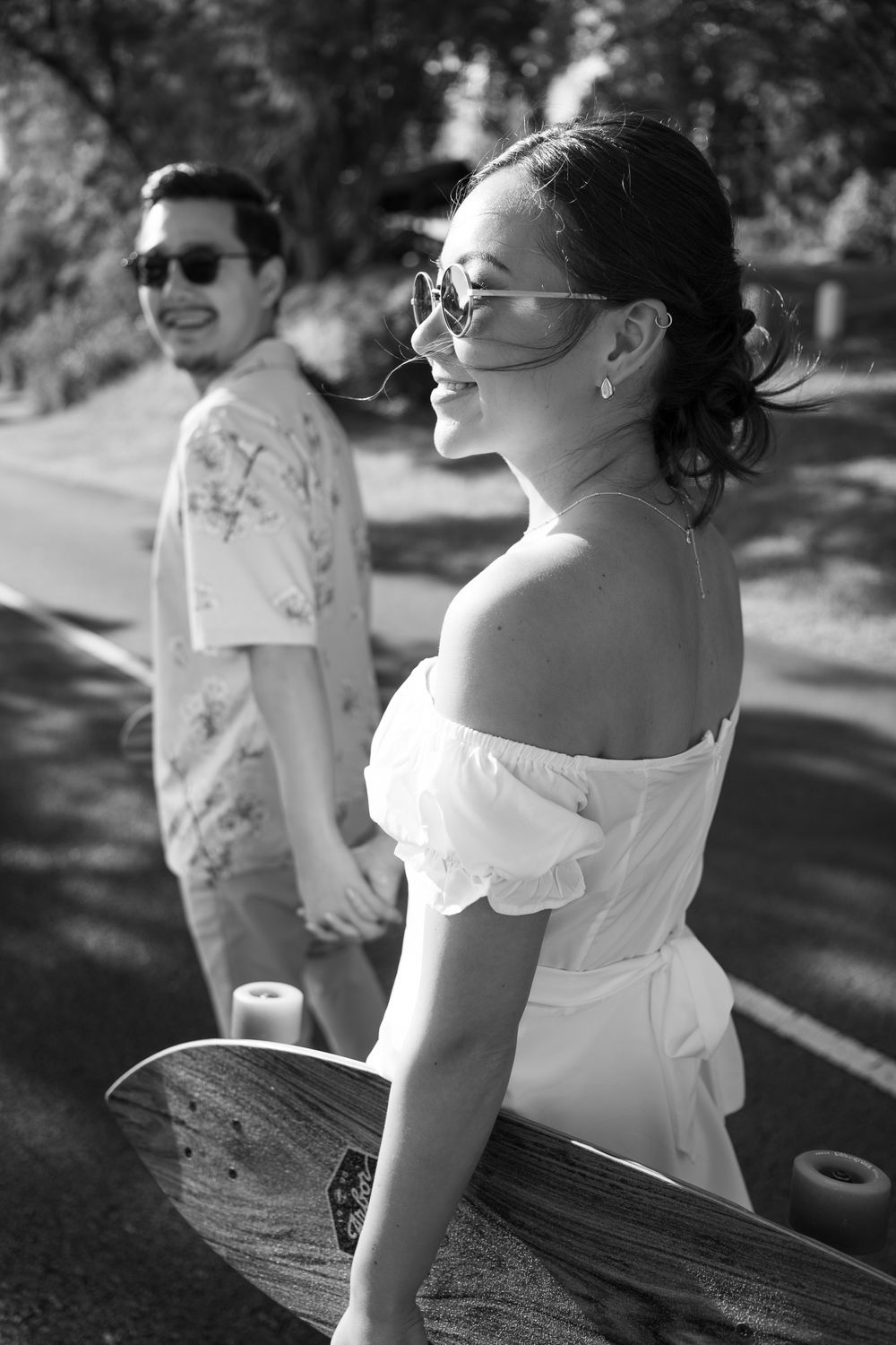 Couple in sunglasses enjoying a sunny day outdoors with longboard in black and white photography.
