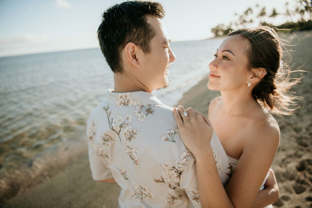 Couple embraces in romantic sunset moment on beach shore with ocean waves in background.