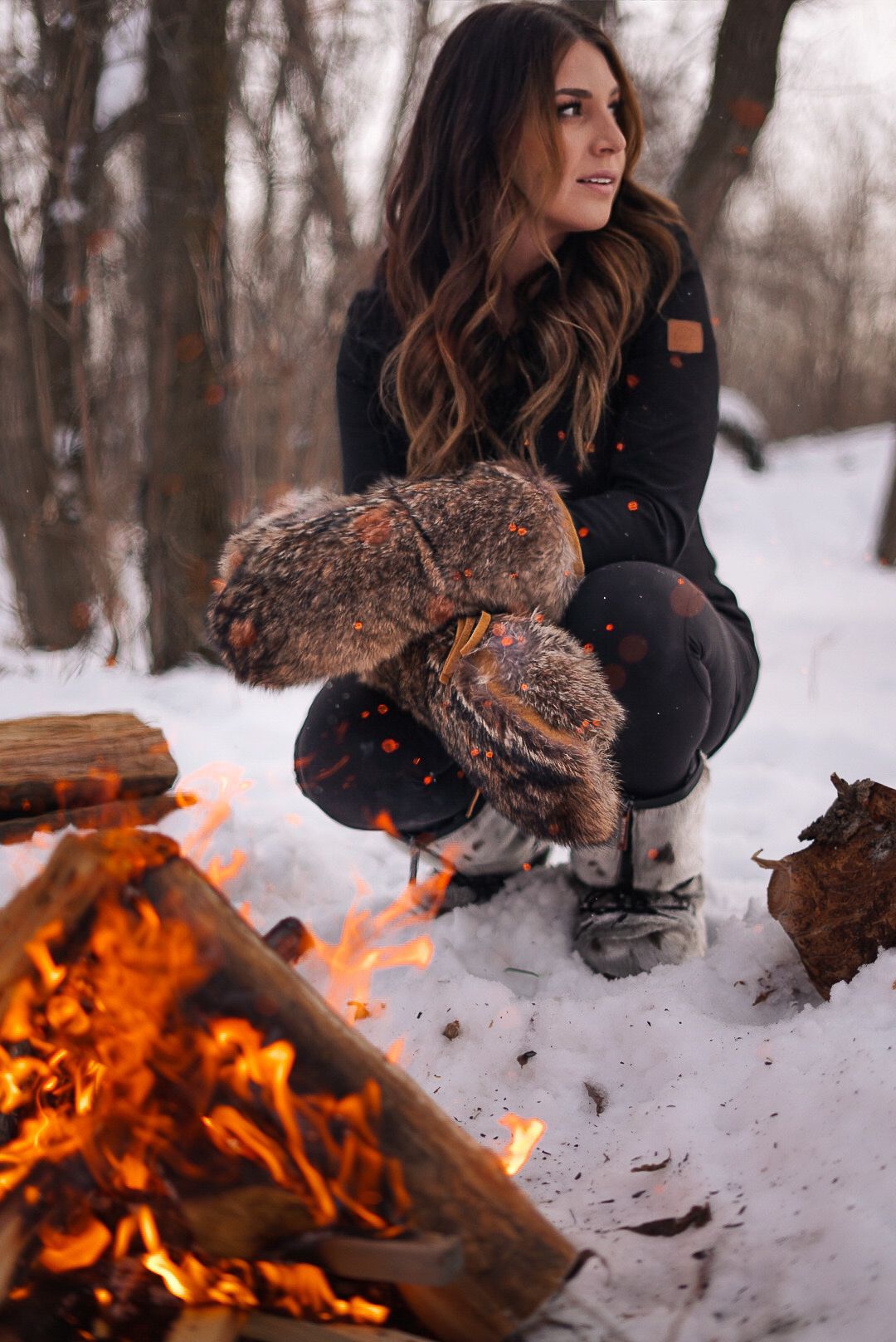Winter scene with person crouching near blazing campfire in snowy forest.