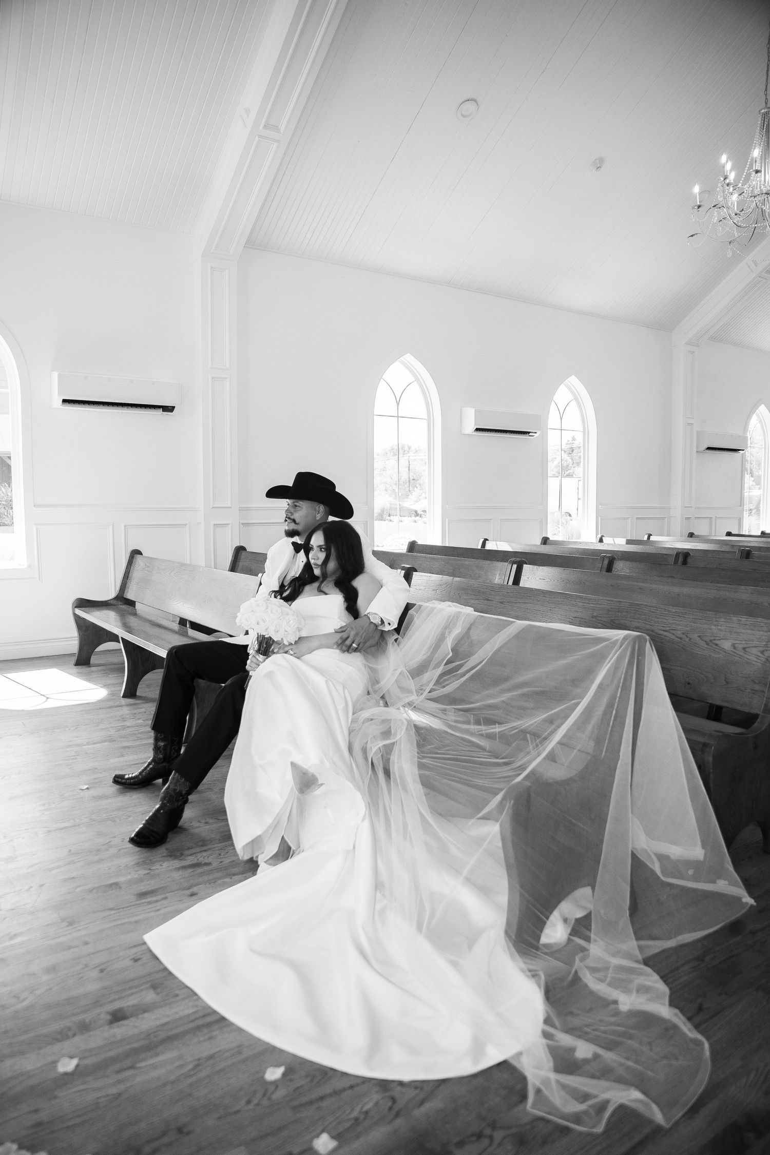 Wedding guests line a walkway as newlyweds exit a white chapel.