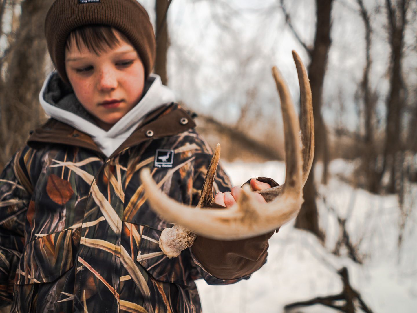 Hunter examining deer antlers in snowy winter forest setting.