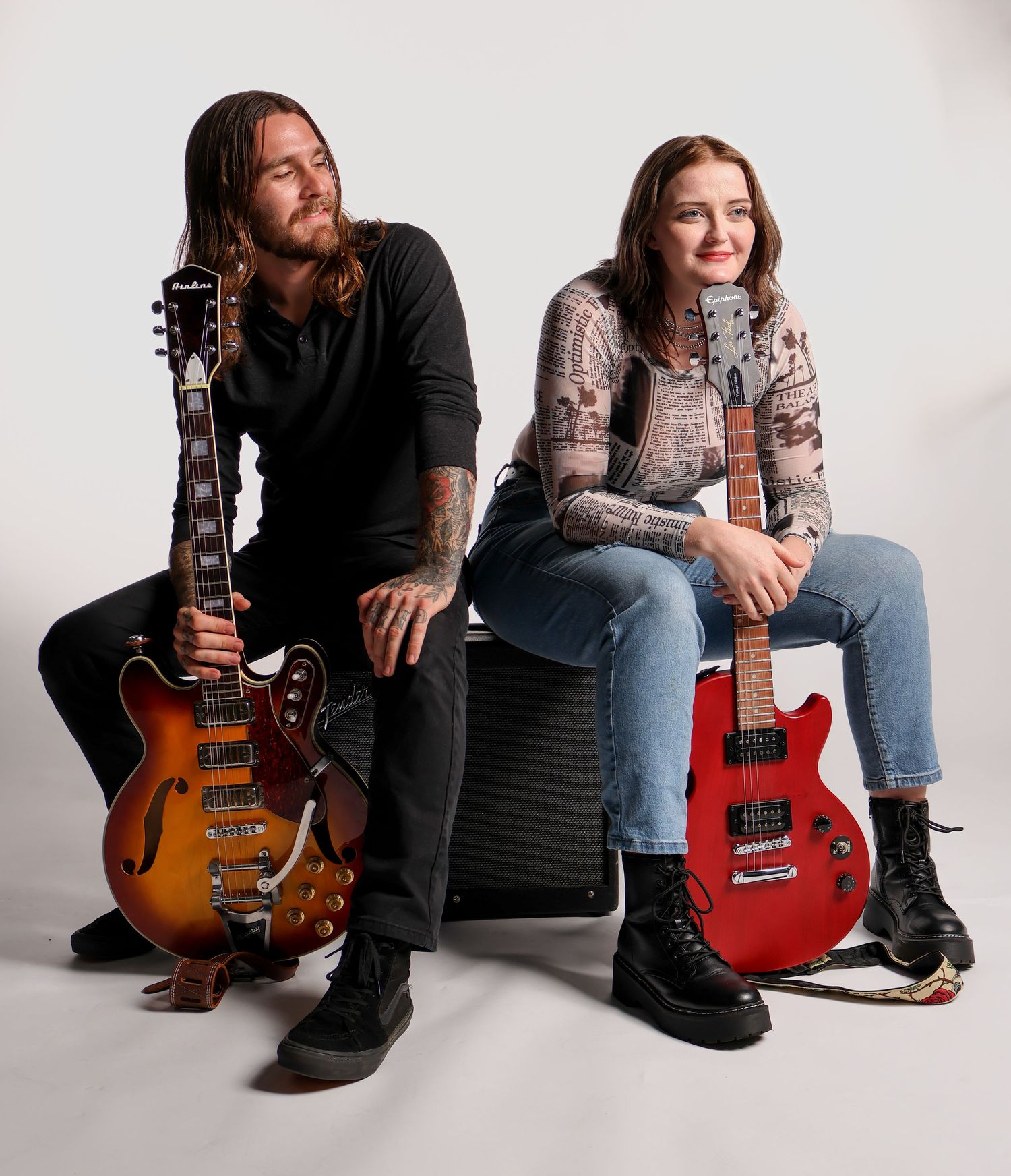 Two musicians pose with electric guitars against a white backdrop in a casual studio portrait.