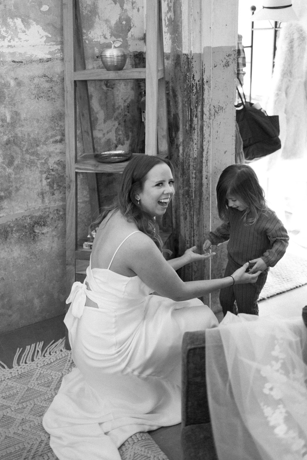 A woman in a white dress kneels and interacts with a small child in a black and white candid moment sussex county nj.