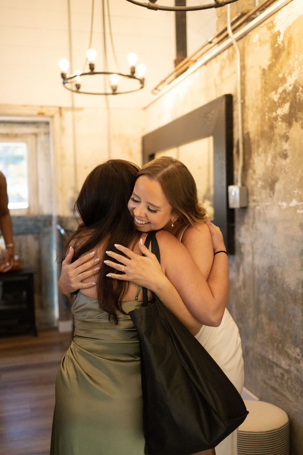 Two women share a warm embrace at an indoor venue with rustic walls and hanging light fixtures near vernon nj.