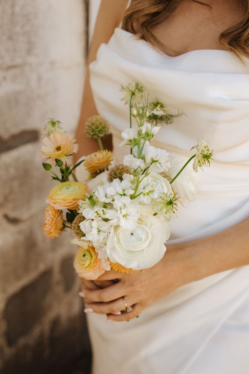 Close-up of a delicate wedding bouquet featuring ranunculus, garden roses and wildflowers against a white gown in sussex county nj.