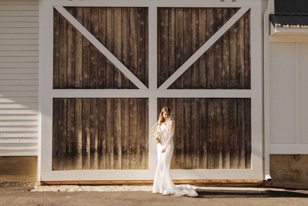 Figure in long white dress stands elegantly against rustic wooden barn doors framed by white trim near vernon nj.