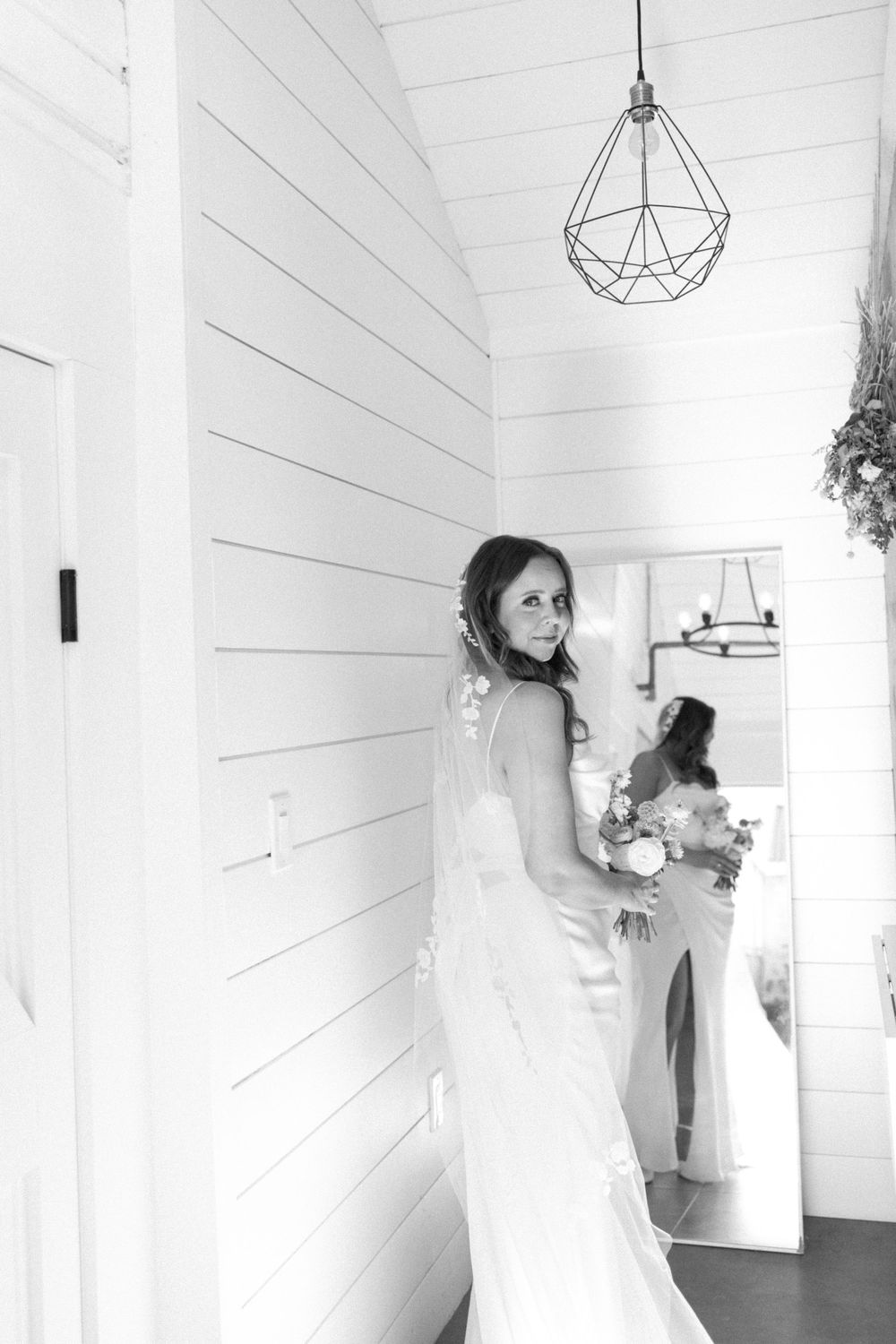 Black and white image showing a bridal figure in a fitted white gown turning in a bright hallway with shiplap walls in sussex county nj.
