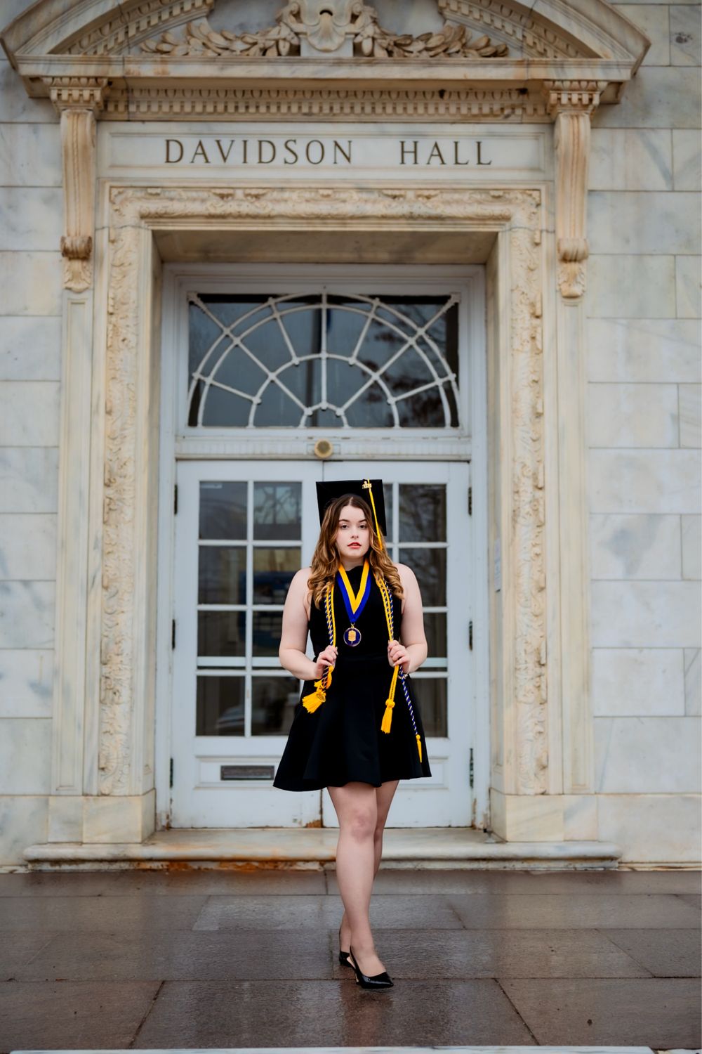 Graduate takes celebratory photos in front of Davidson Hall's classical architecture.