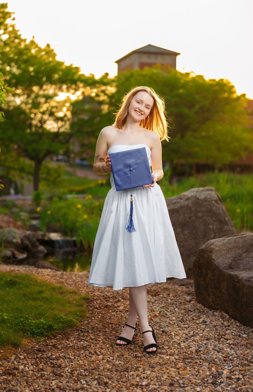 A graduation photo series featuring a light blue dress and navy diploma holder on rocky terrain.