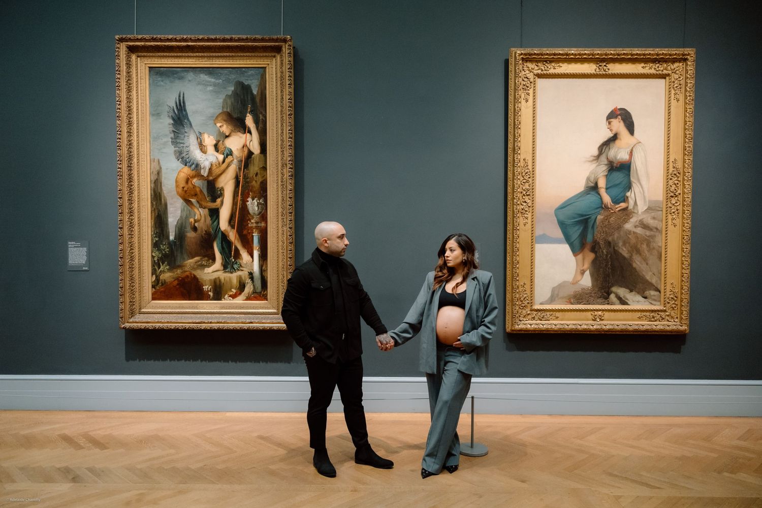 A couple holds hands in an art museum, with the expectant mother’s pregnant belly gently exposed, blending intimacy with artistic ambiance.