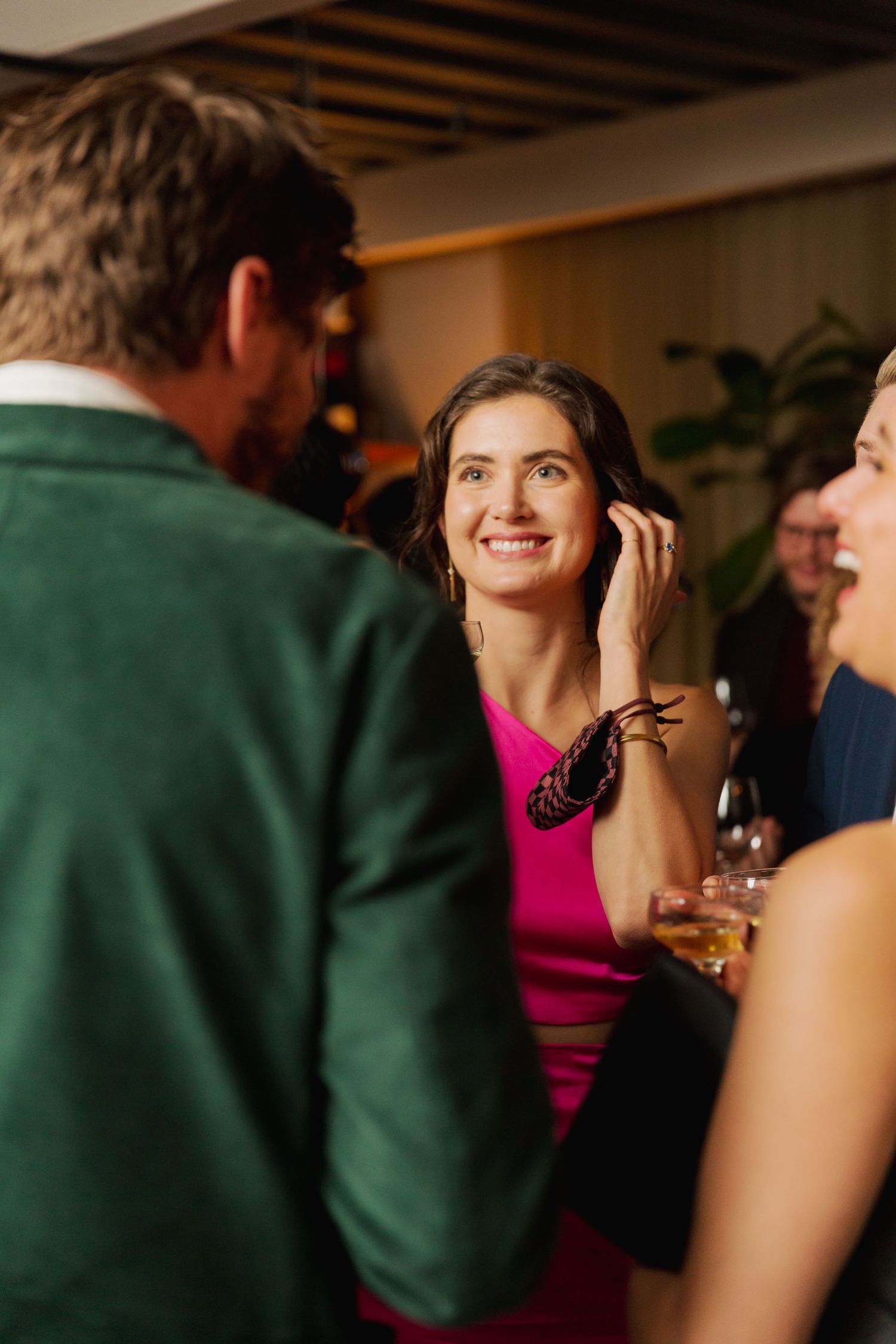 A group of people engaged in conversation at a social gathering, with someone wearing a bright pink dress in the center.
