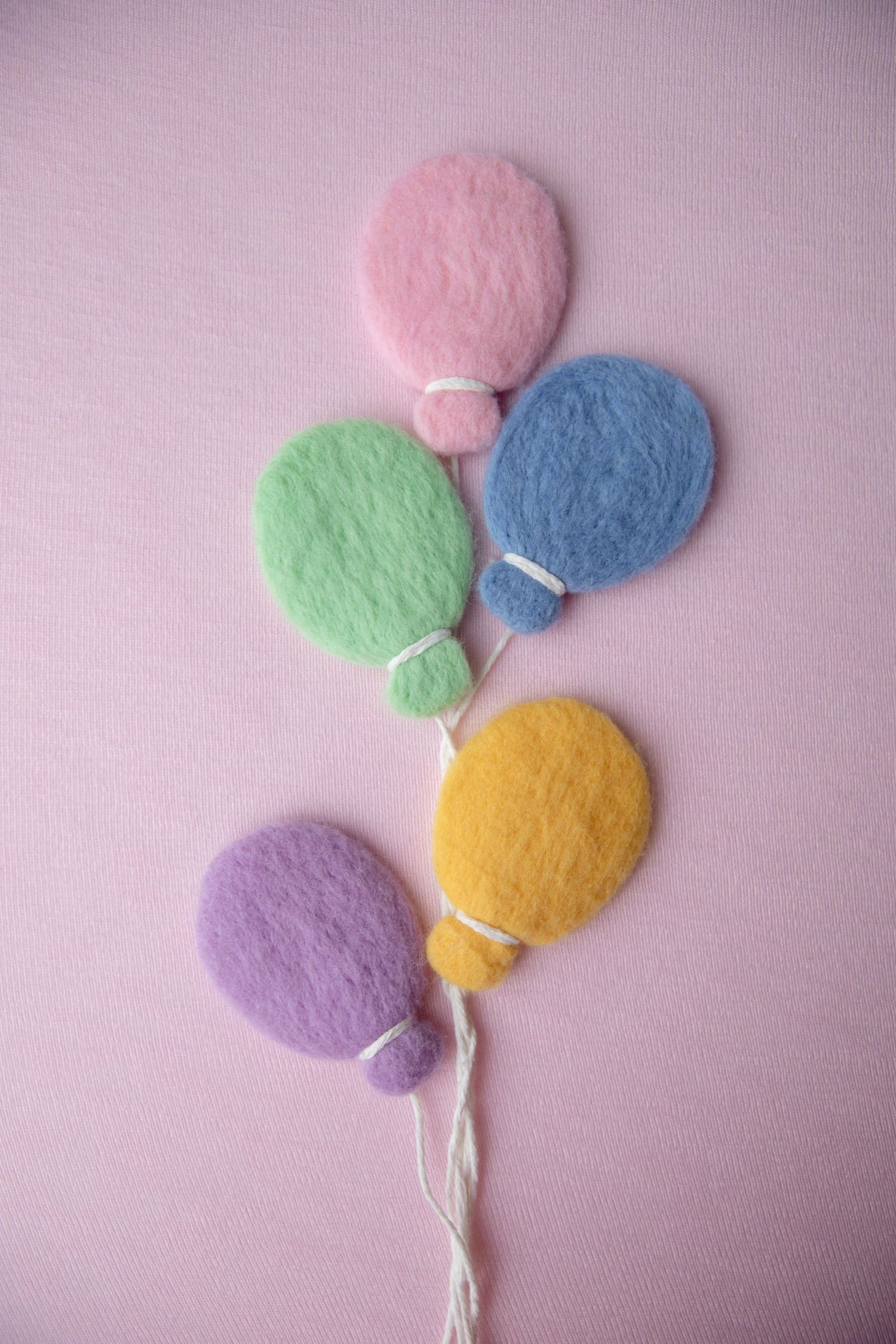 Five pastel felt balloons in pink, green, blue, yellow, and purple on pink background.