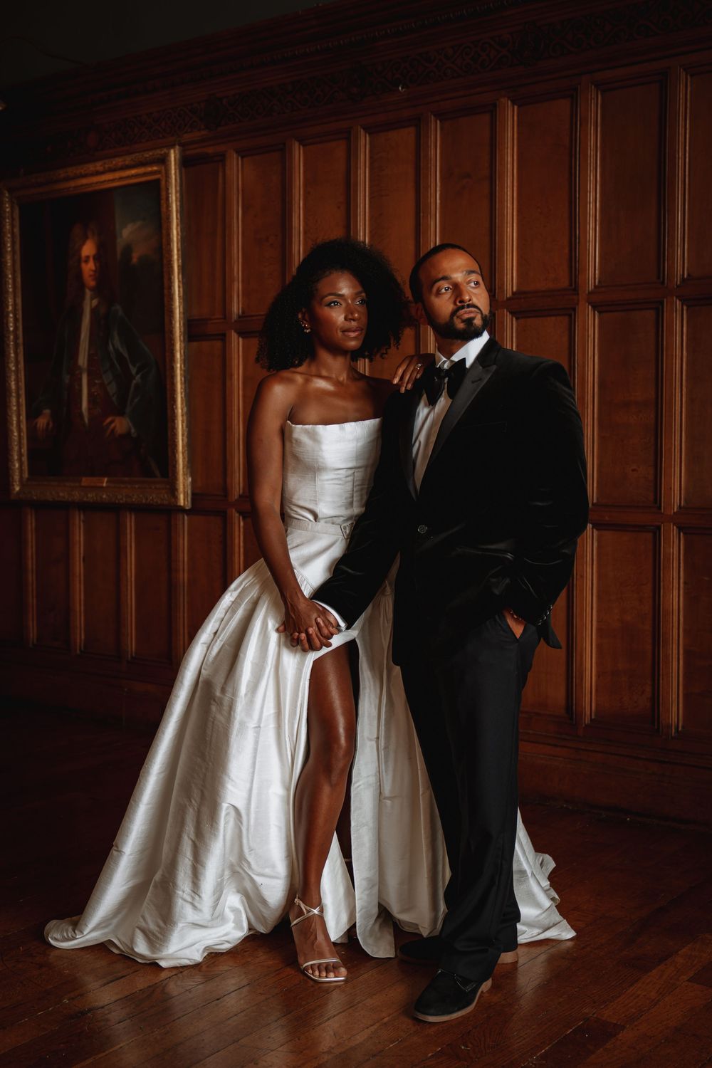 Elegant couple in white satin wedding gown with slit and black velvet tuxedo posing at Arley Hall