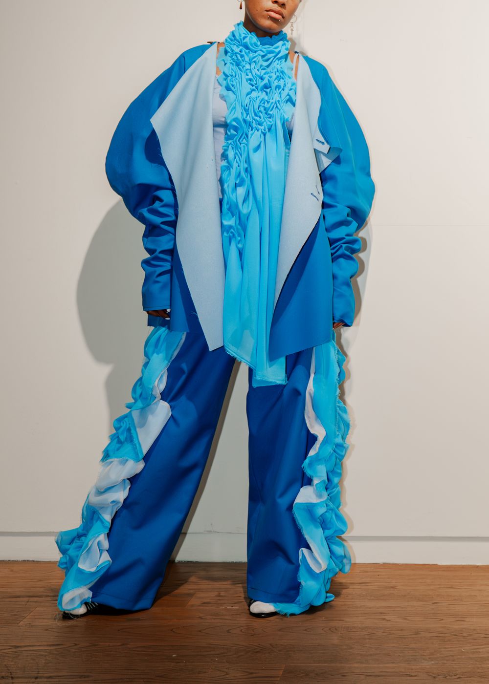 Model wears bold blue ruffled oversized jacket with wide-leg pants ensemble. University fashion show at Manchester art gallery